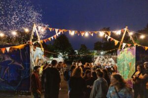 Sommerfest im Kulturhaus. feiernde Menschen draußen im bunt beleuchteten Containerbereich am Kulturhaus-Eingang.