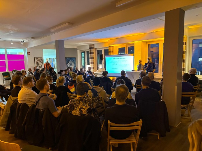 Eine große Gruppe lauscht einem Vortrag mit Präsentation